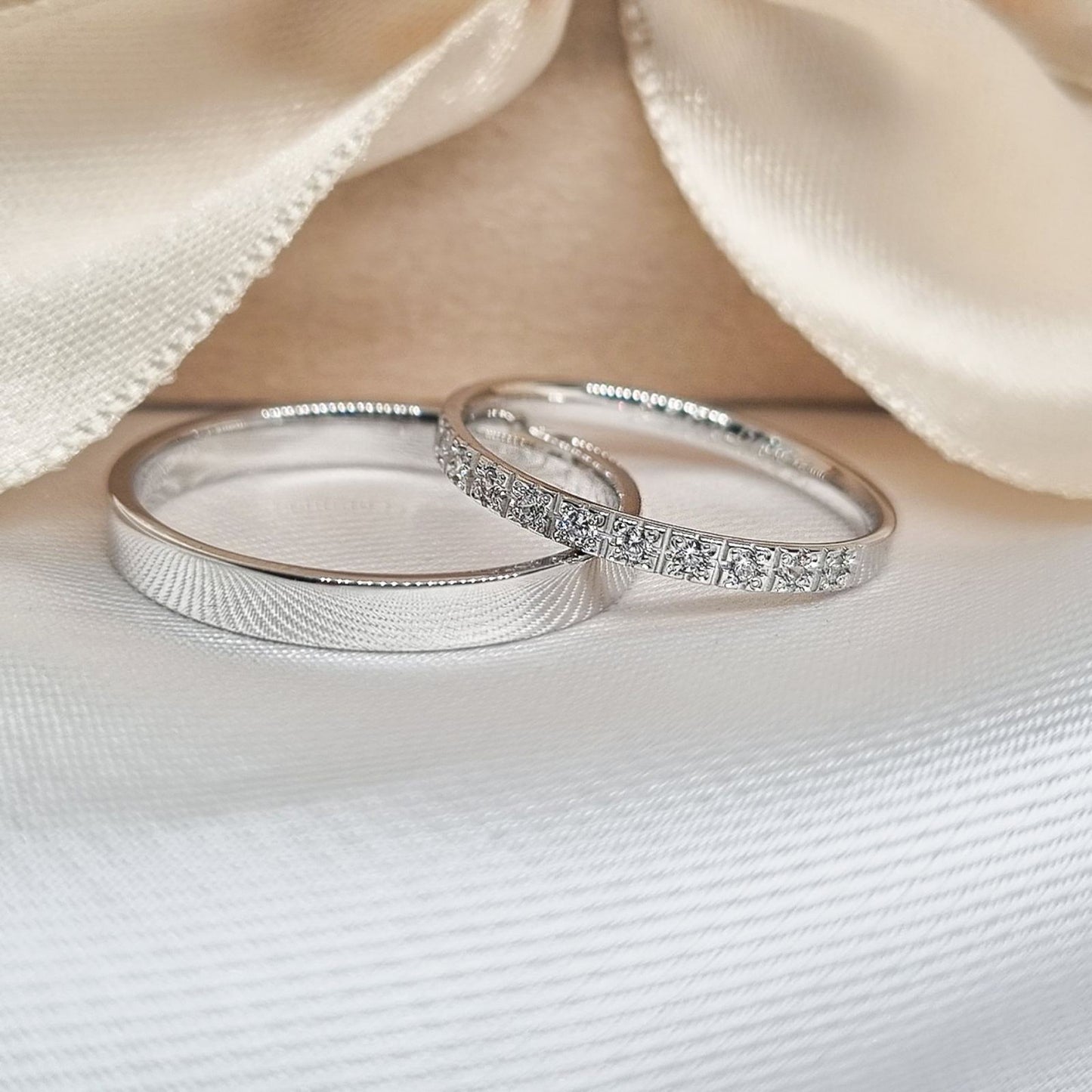 Par burmi od belog zlata, od kojih je ženska ukrašena redom sitnih cirkona koji nežno sijaju, dok je muška burma jednostavna, položenih na svetlu podlogu uz svilenu mašnu u pozadini