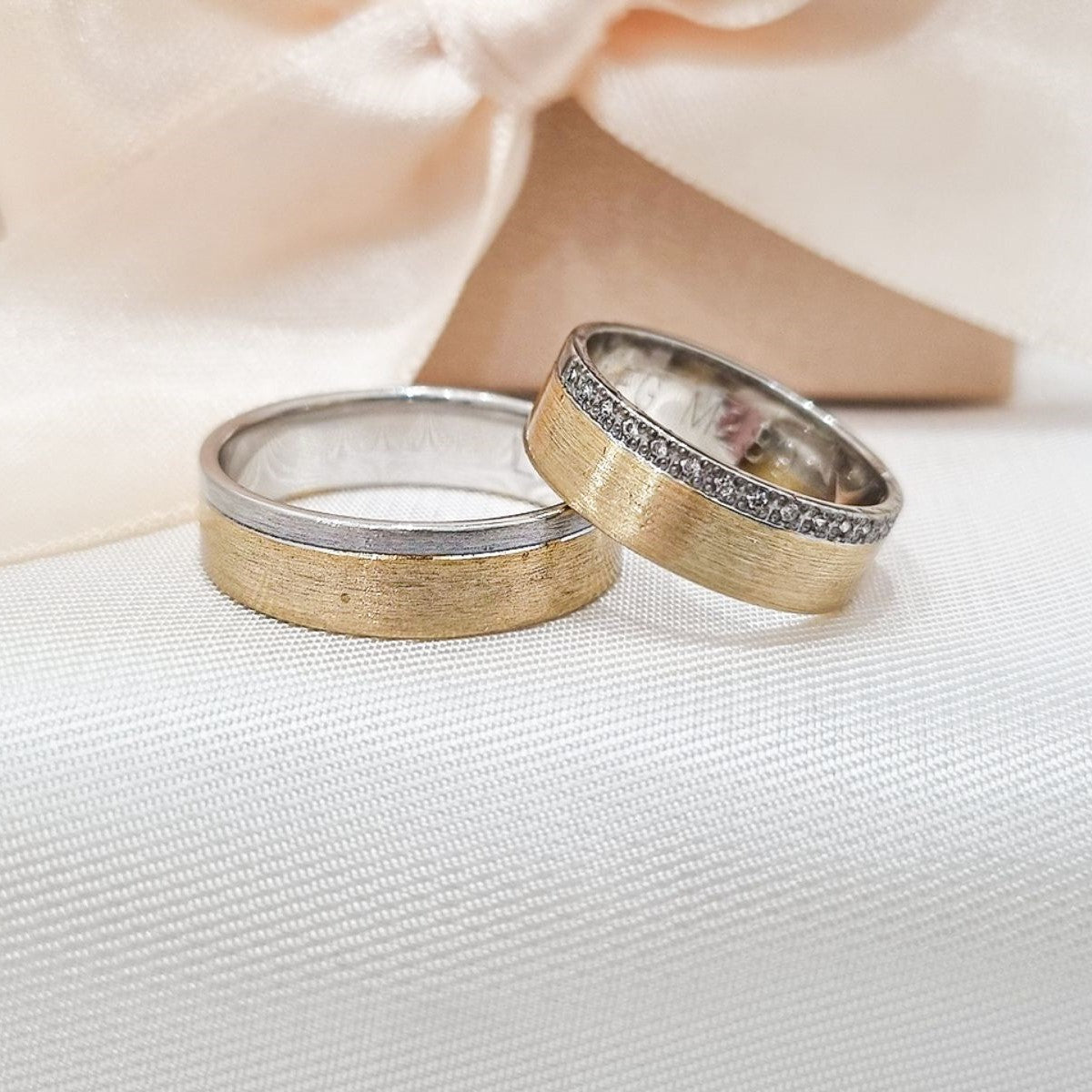 Burme od belog i žutog zlata, jedna ukrašena cirkonima u gornjem delu, položene na belu svilenkastu tkaninu.