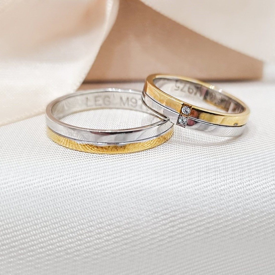 Zlatne burme u kombinaciji belog i žutog zlata sa dijamantima na jednoj burmi, postavljene na mekoj bež tkanini sa svetlom pozadinom.