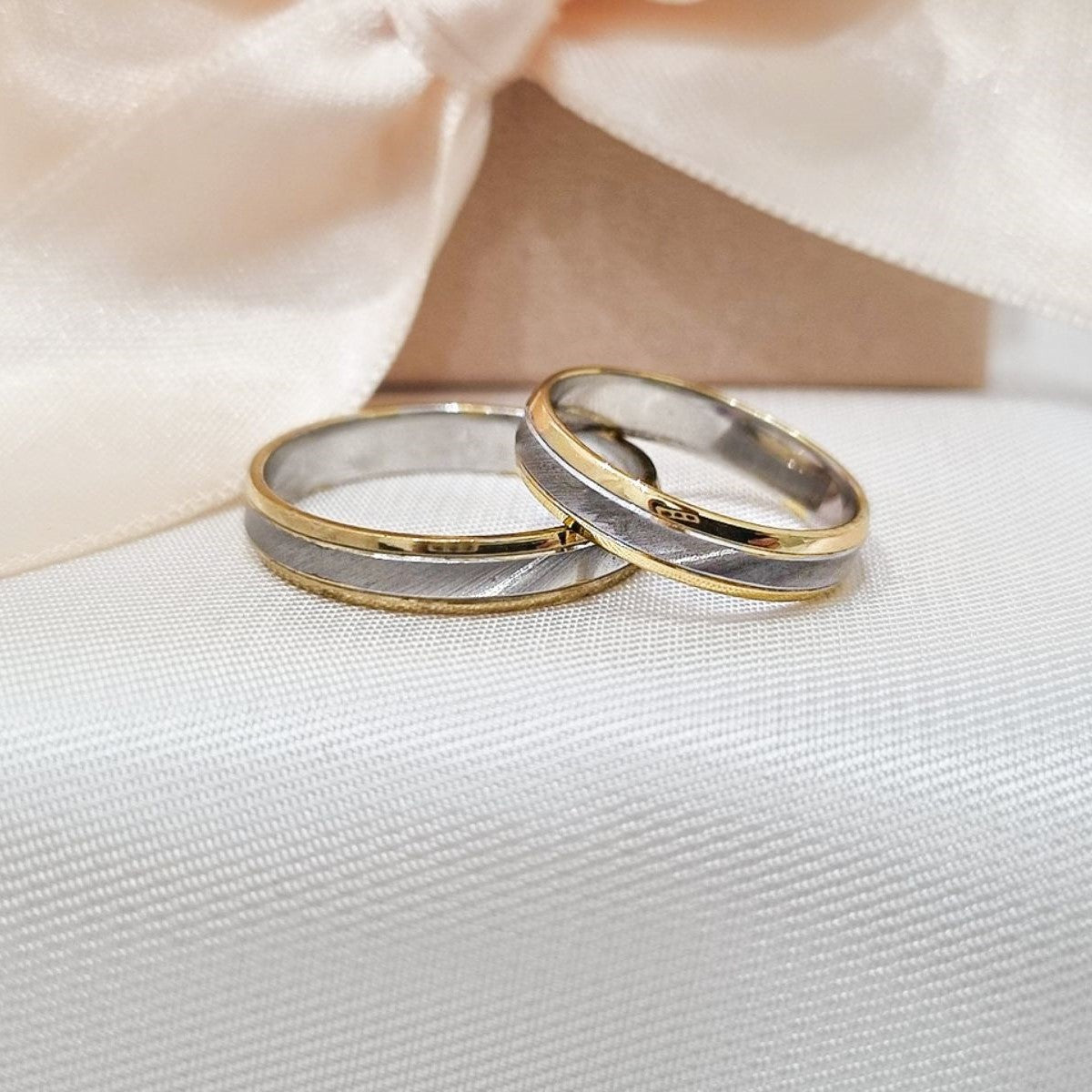 Zlatne burme sa kombinacijom žutog i belog zlata, postavljene na bež tkanini sa svetlom pozadinom.