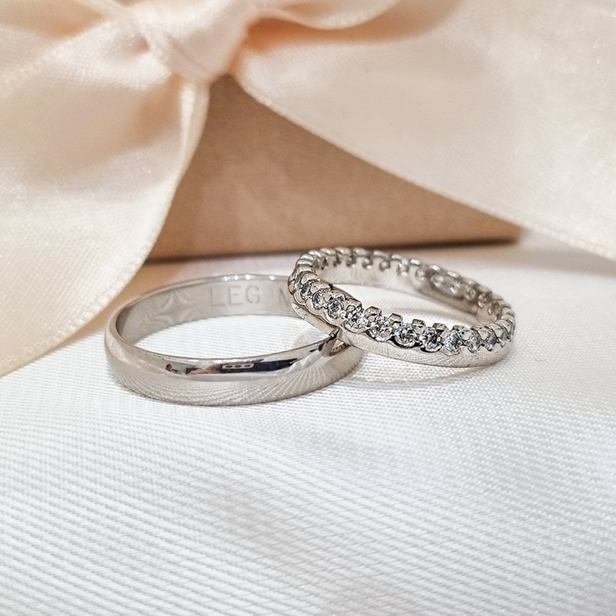 Burme od belog zlata – jedna glatka i sjajna, druga u potpunosti ukrašena cirkonima, fotografisane na beloj podlozi uz satensku mašnu.