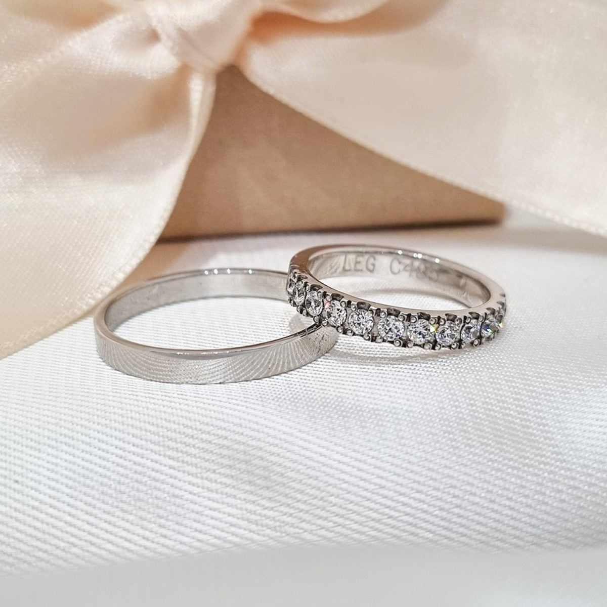 Burme od belog zlata, jednostavna mat muška i ženska sa cirkonima, postavljene na beloj tkanini uz dekorativnu mašnu.