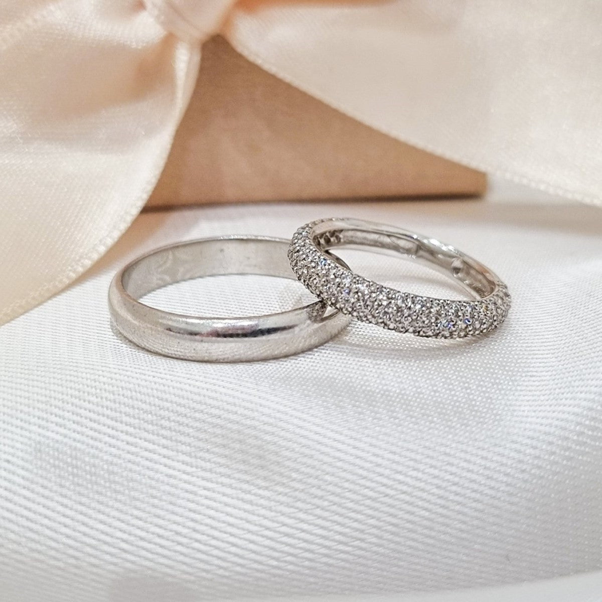 Zlatne burme, jedna sa glatkom površinom, dok je druga potpuno ukrašena cirkonima, postavljene na bež tkanini sa svetlom pozadinom.