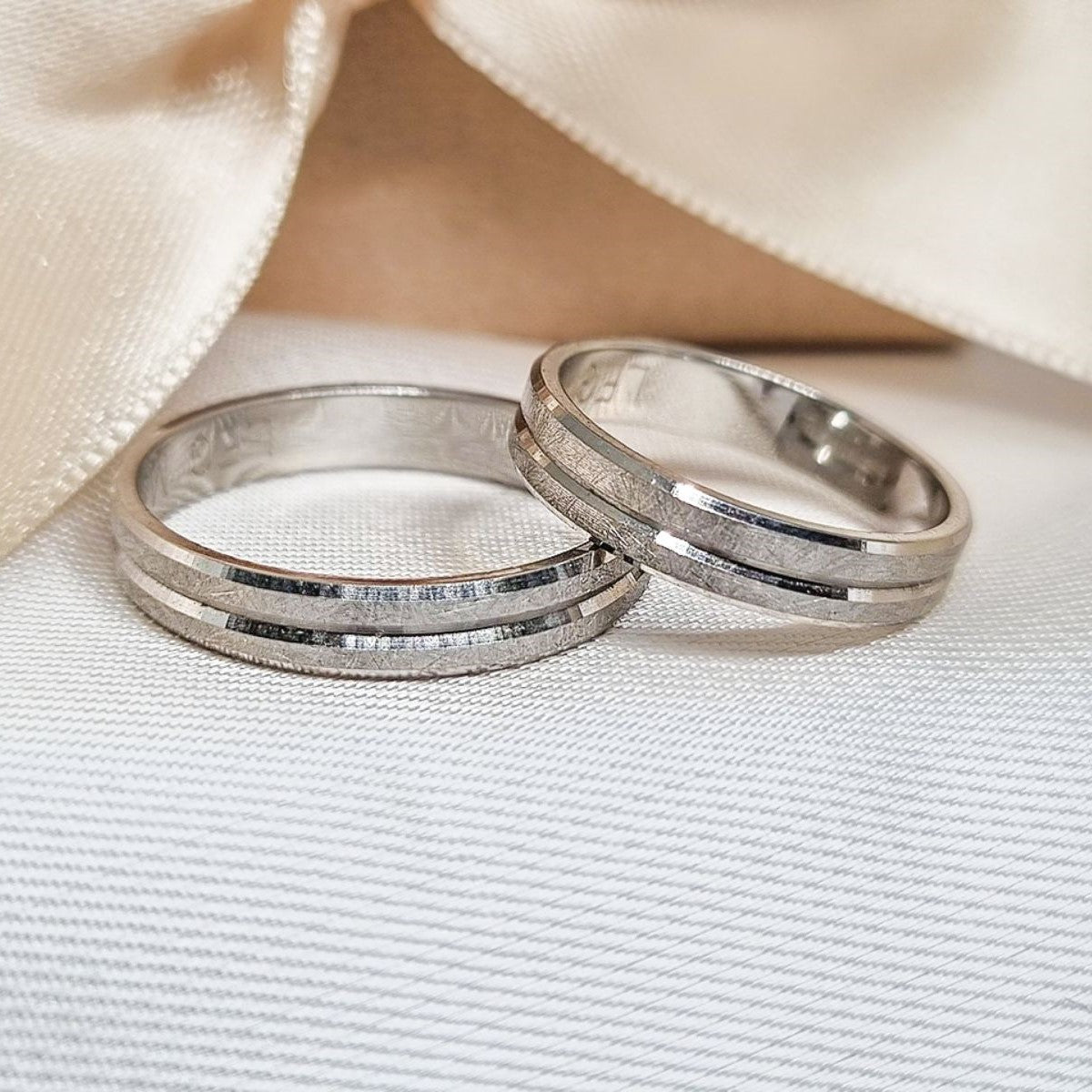 Par burmi od belog zlata sa duplim središnjim linijama u mat finišu i sjajnim bočnim ivicama, položene na svetloj tkanini ispred satenske mašne.