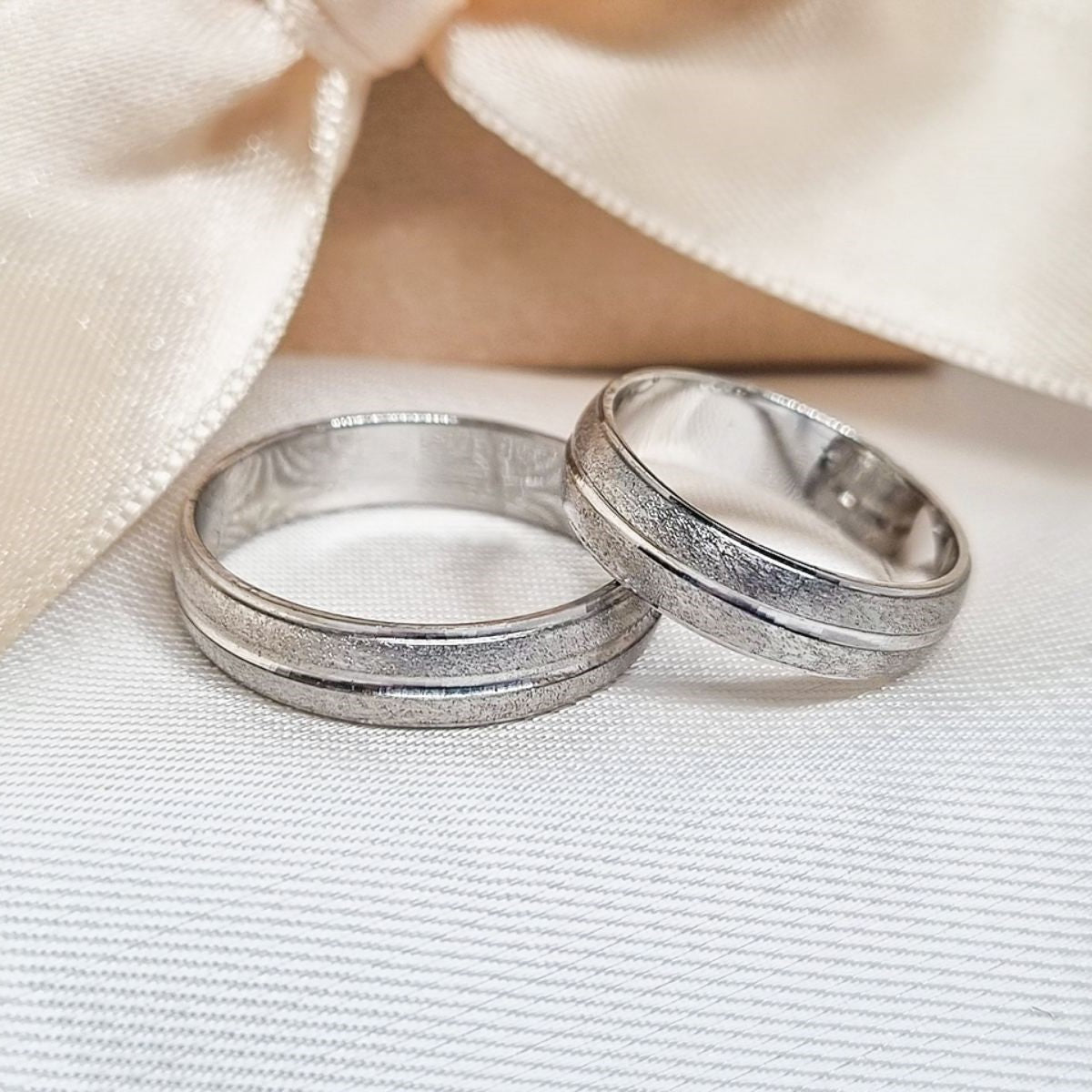 Burme belo zlato sa linijom i peskiranom završnicom, postavljene na beloj pozadini, sa nežnom mašnom