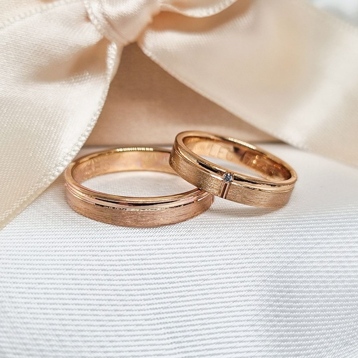 Burme od roze zlata sa mat efektom, ženska burma ukrašena jednim cirkonom, prikazane na beloj podlozi ispred svilene mašne.