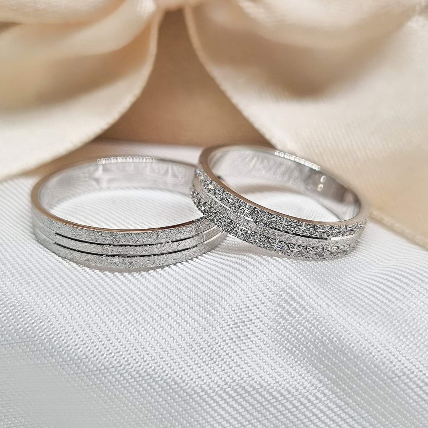 Zlatne burme sa matiranim i poliranim detaljima, jedna ukrašena cirkonima, postavljene na bež tkanini sa svetlom pozadinom.