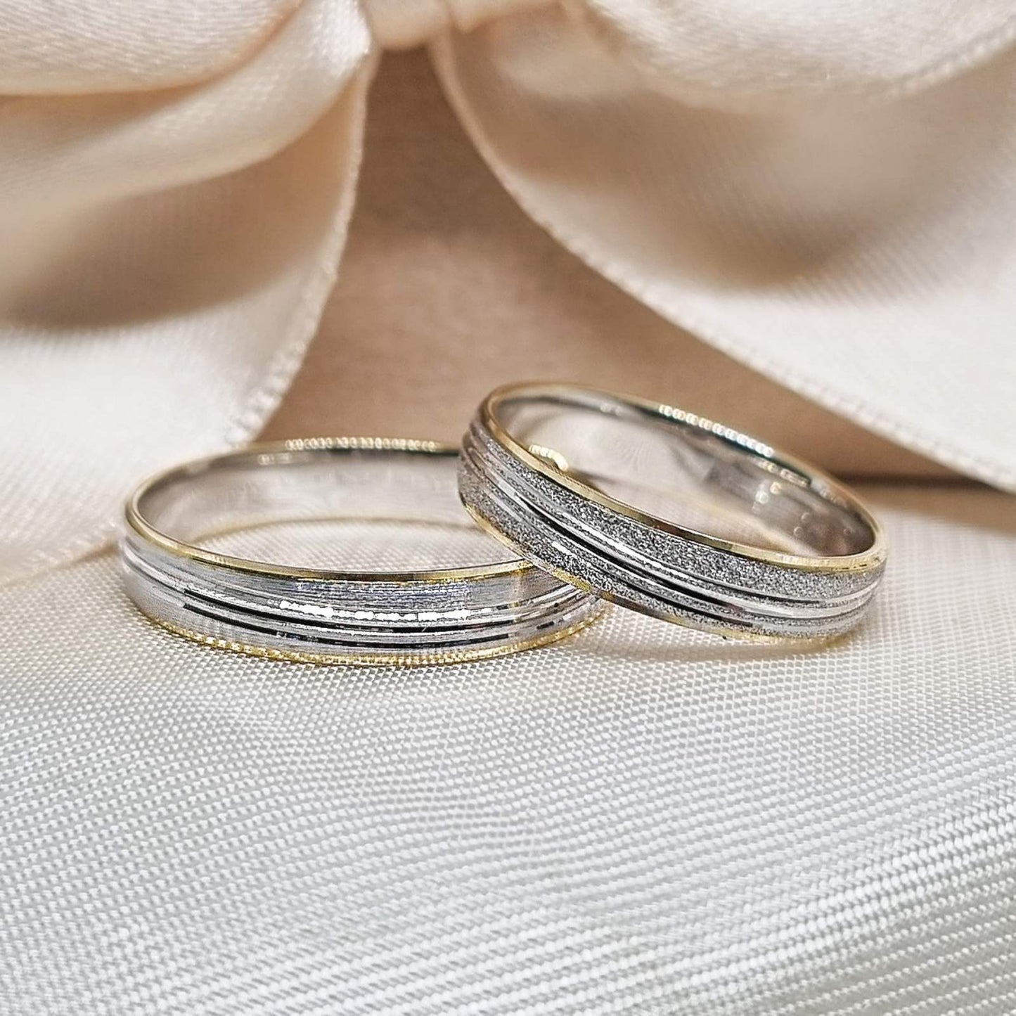 Zlatne burme sa kombinacijom žutog i belog zlata, matiranim i poliranim detaljima, postavljene na bež tkanini sa svetlom pozadinom.