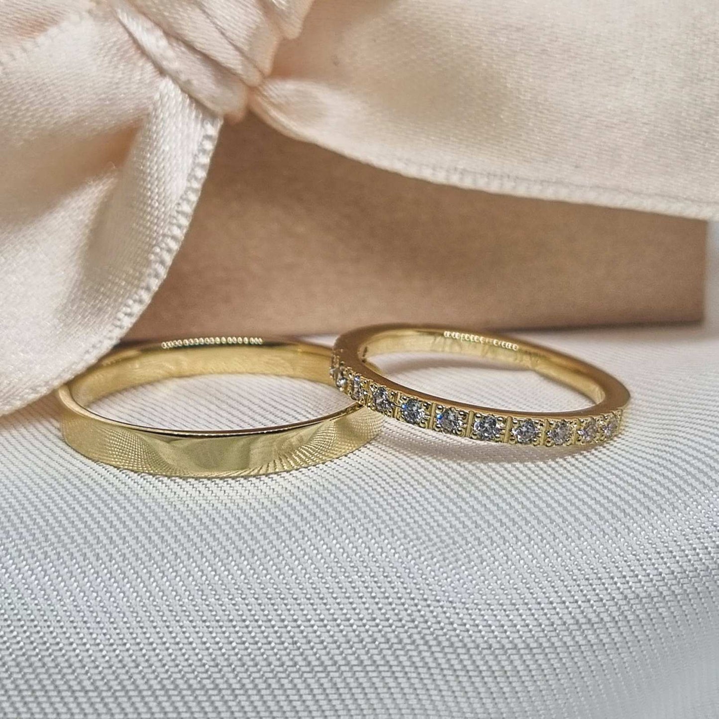 Dve zlatne burme na svetloj, teksturiranoj pozadini. Jedna burma sa glatkom zlatnom površinom, a druga sa cirkonima postavljenim na vrhu.