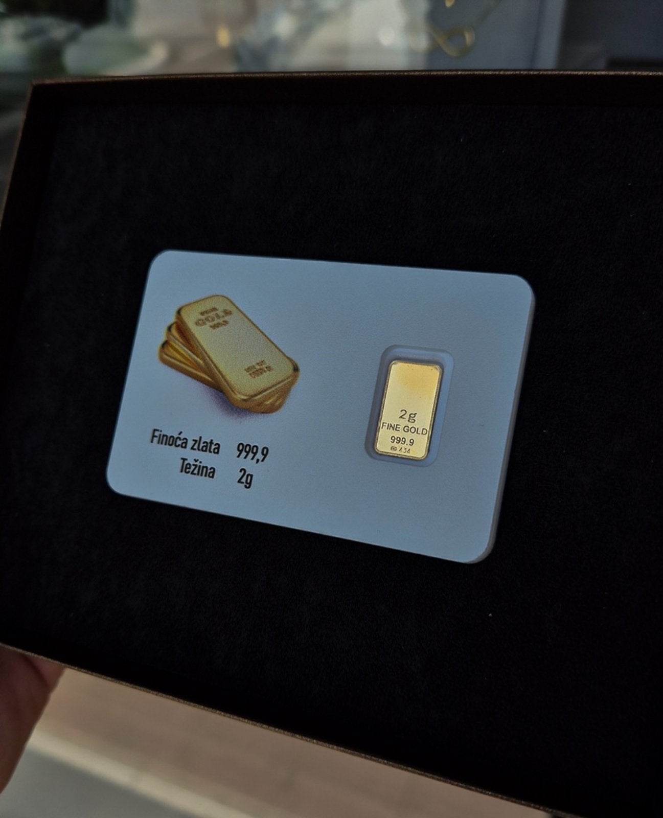 Zlatna poluga težine 2 grama i finoće 999,9 prikazana unutar zaštitne plastične kartice na tamnoj, crnoj pozadini.