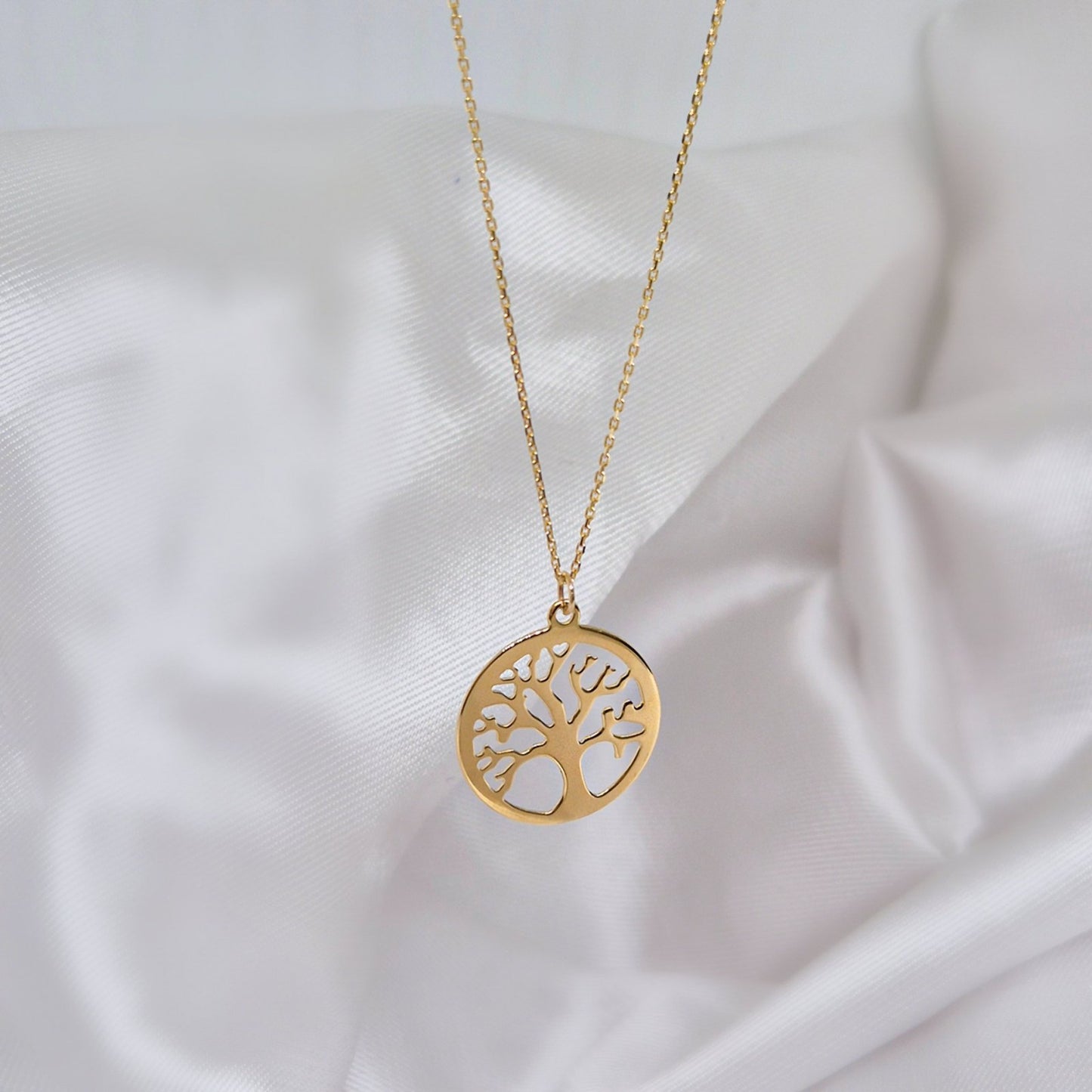 Zlatna ogrlica sa priveskom u obliku drveta života izrezanog u krugu.