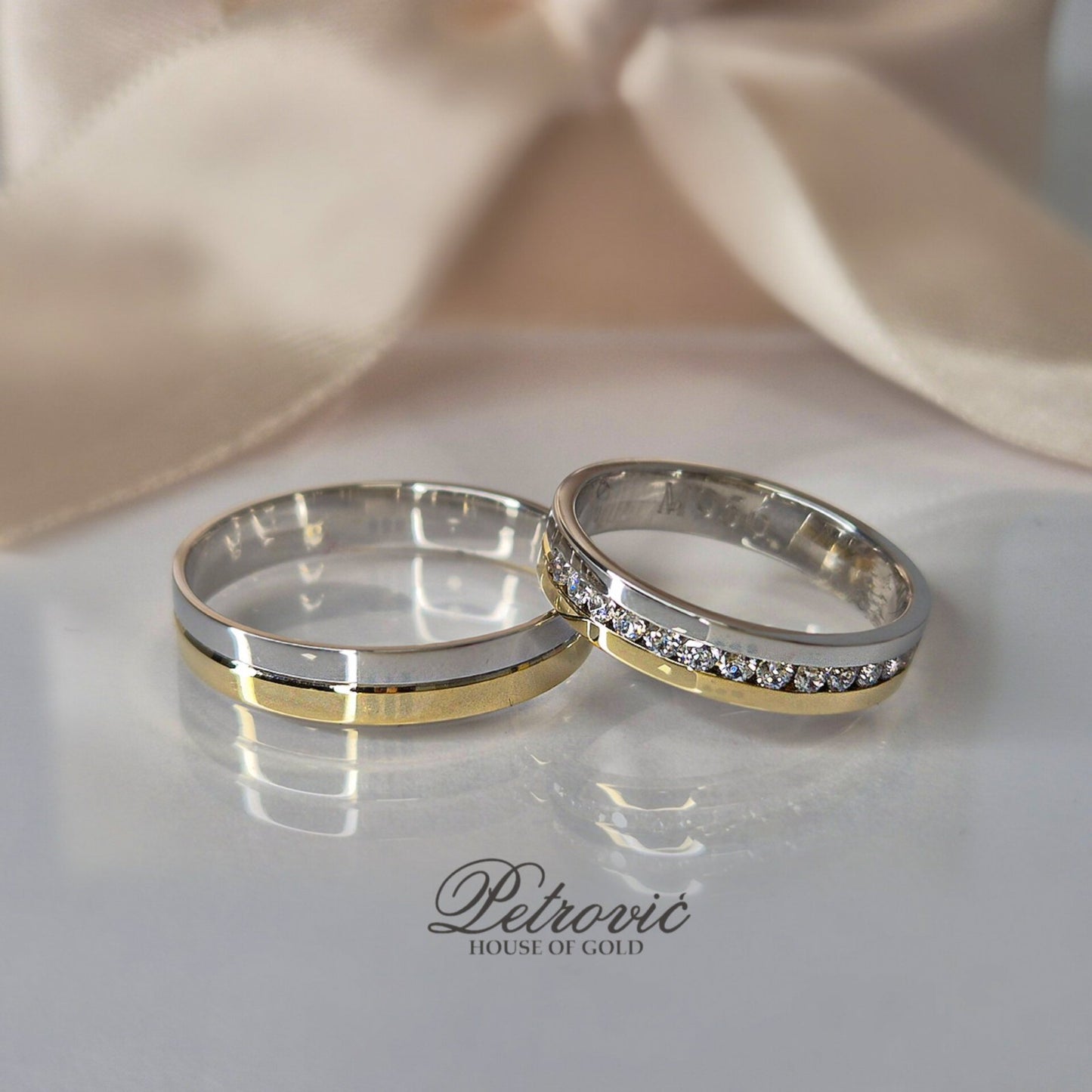 Par zlatnih burmi u kombinaciji belog i žutog zlata, ženska burma sa redom cirkona, postavljene na sjajnoj beloj podlozi sa satenskom pozadinom u bež nijansi.