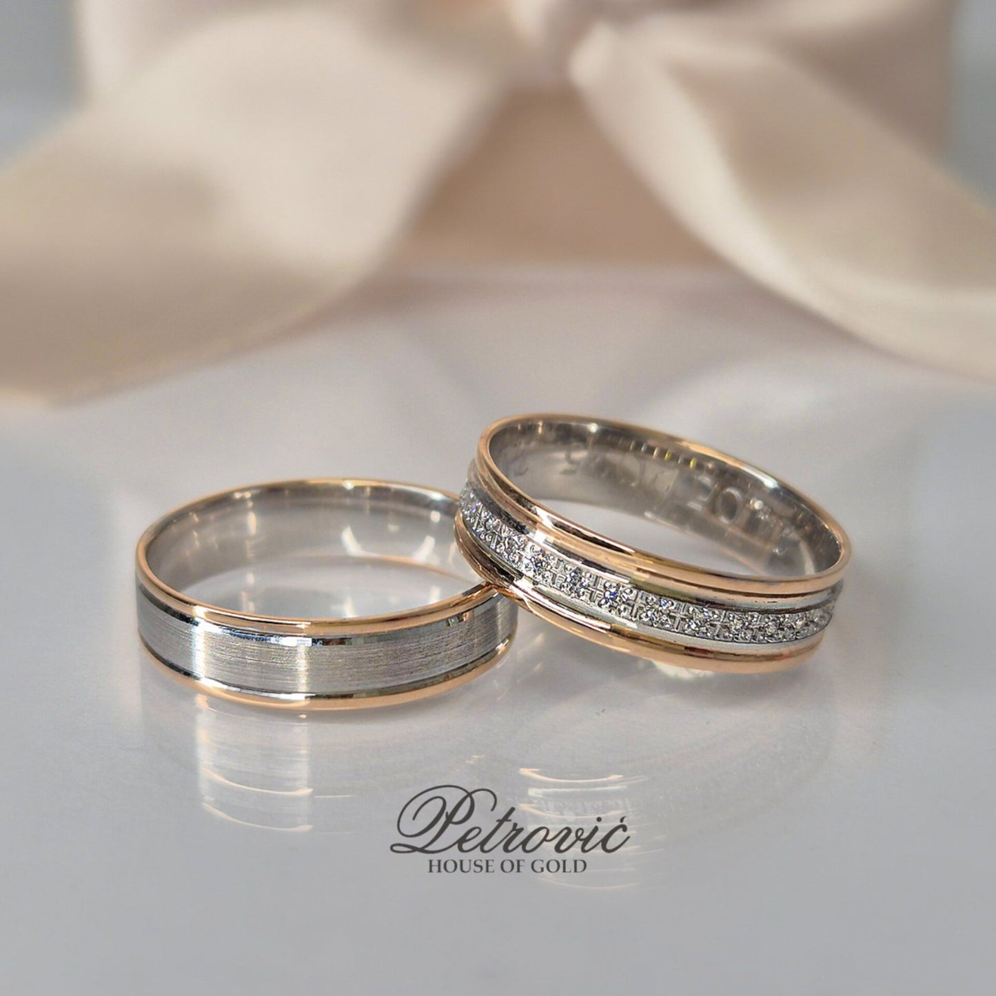 Par burmi od belog i roze zlata, muška sa mat središnjim delom, ženska ukrašena cirkonima u nizu, postavljene na sjajnoj beloj podlozi sa bež pozadinom.