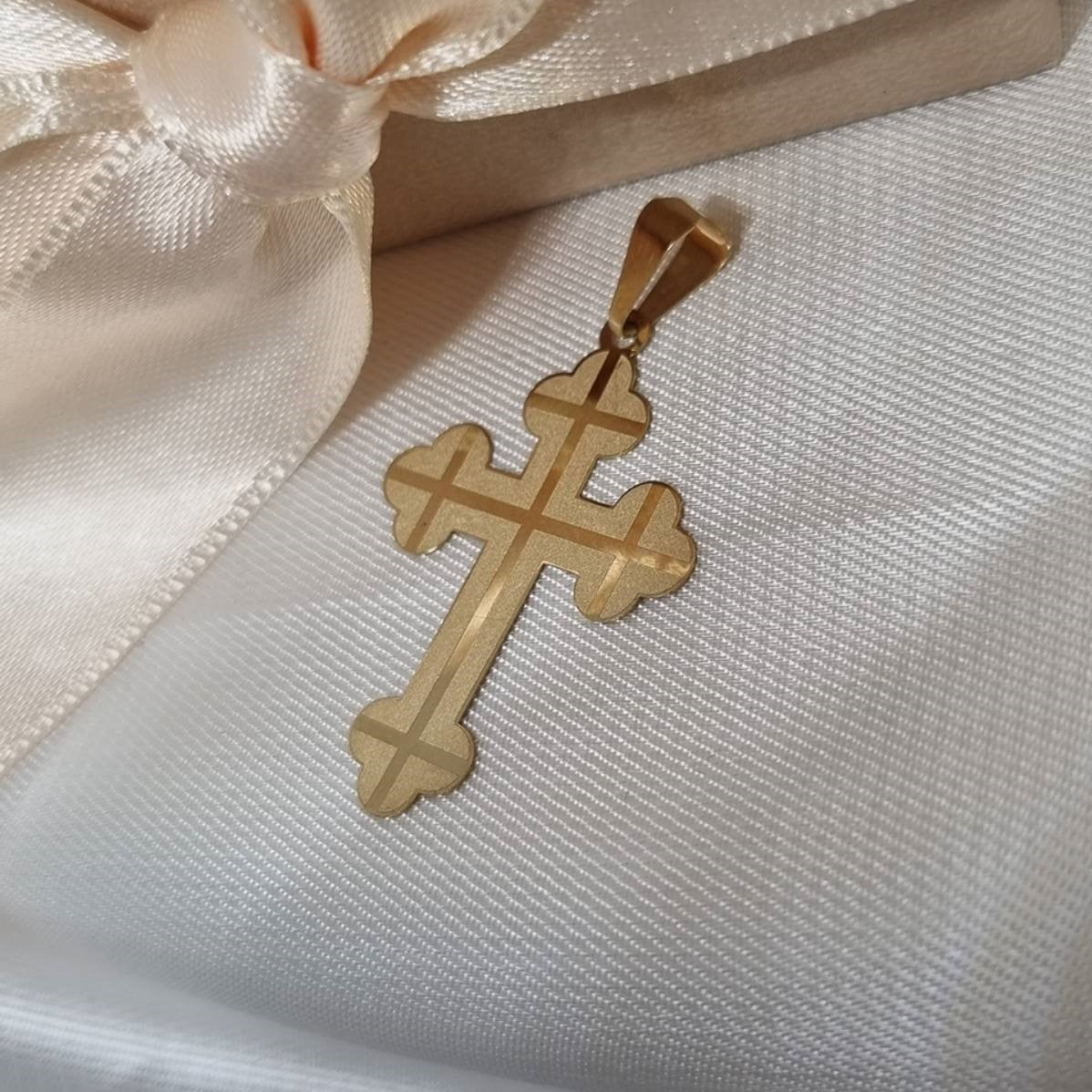 Zlatni pravoslavni krstić sa ukrasnim krajevima i ugraviranim sjajnim linijama.