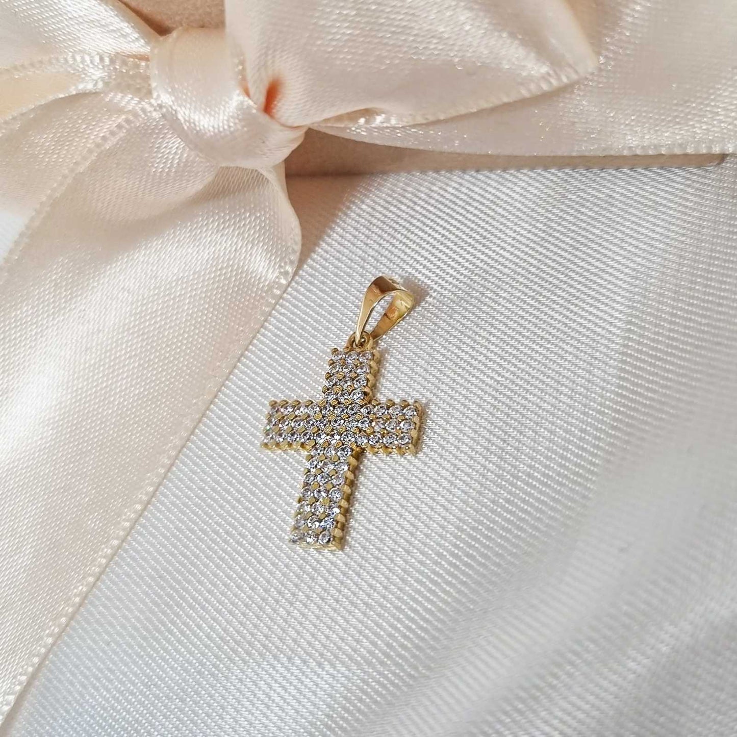 Zlatni krst privezak u potpunosti prekriven cirkonima, na beloj svilenoj podlozi.