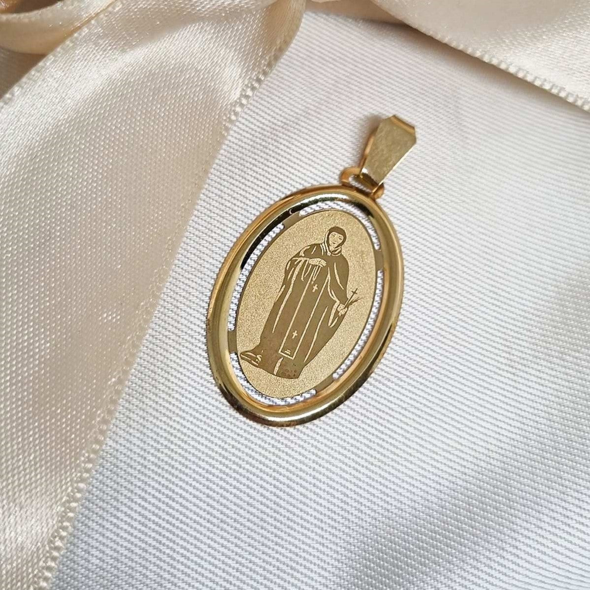 Zlatni ovalni privezak sa likom Svete Petke prikazan na bež pozadini