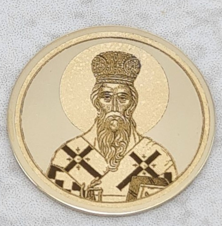 Zlatnik sa ugraviranim likom Svetog Vasilija Ostroškog, sa mitrom na glavi i dugom bradom, drži evanđelje, prikazan na sivoj pozadini.