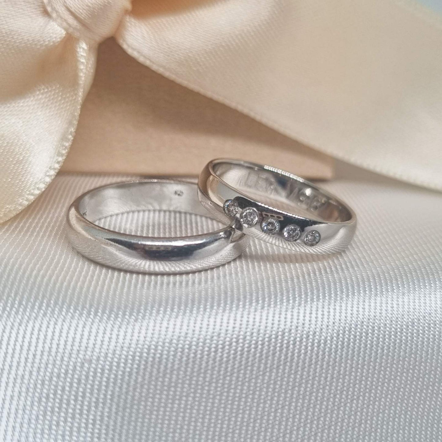 Burme od belog zlata sa glatkom završnom obradom, jedna ukrašena sa pet sitnih cirkona, fotografisane na svilenoj podlozi.