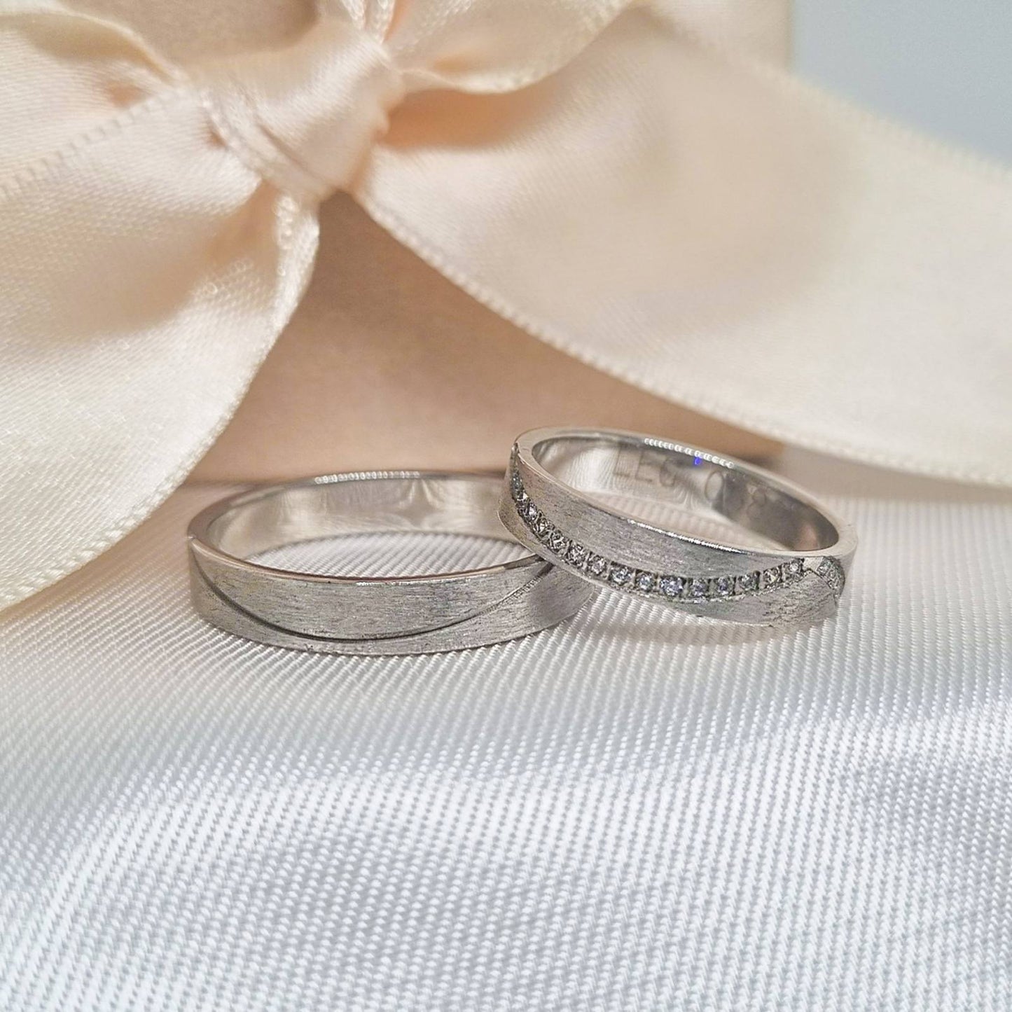 Burme belo zlato sa krivom linijom, postavljene na bež tkanini sa svetlom pozadinom.