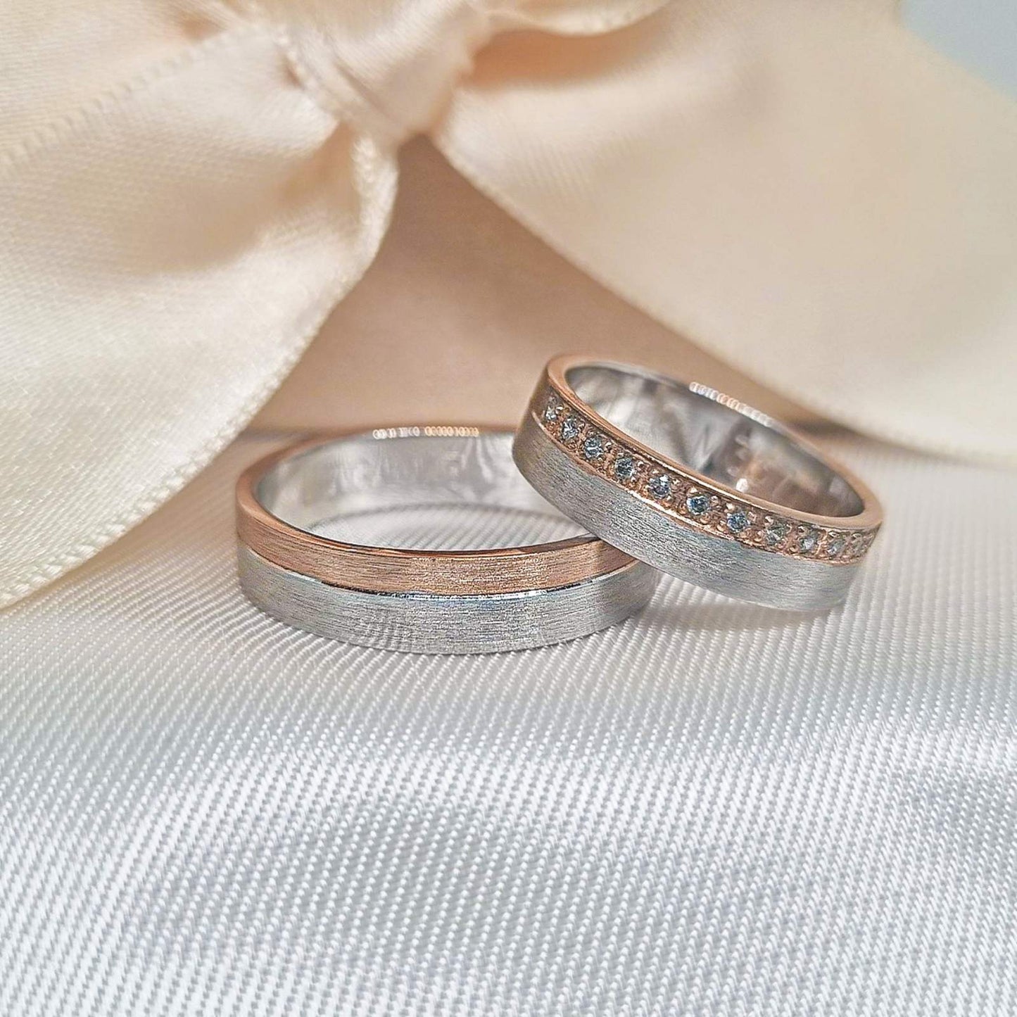 Par burmi od belog i roze zlata, ženska burma sa cirkonima, na svetloj tekstilnoj podlozi ispred dekorativne mašne.