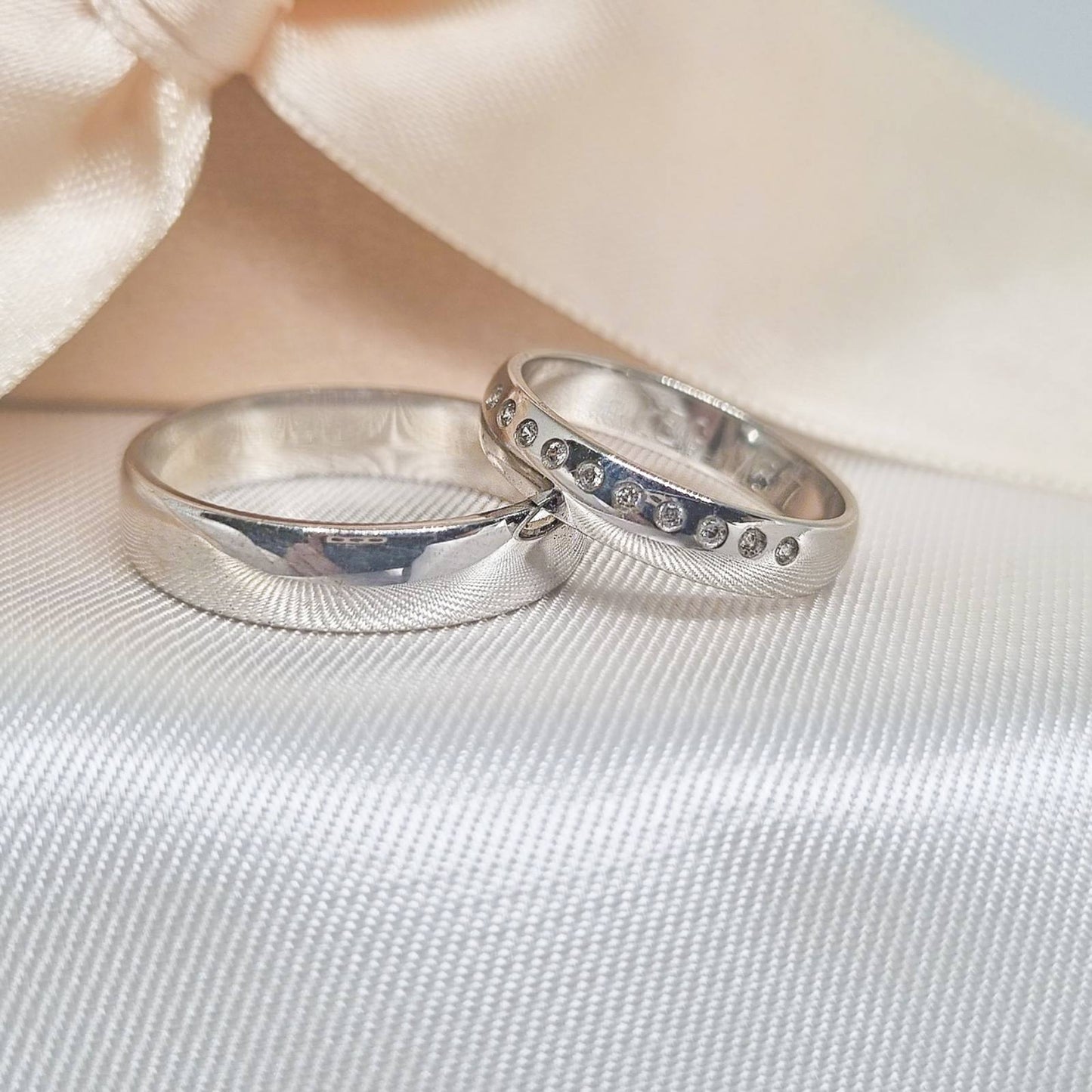 Zlatne burme od belog zlata sa poliranom završnicom, jedna ukrašena redom cirkona, postavljene na svetlu tkaninu sa satenskom pozadinom.