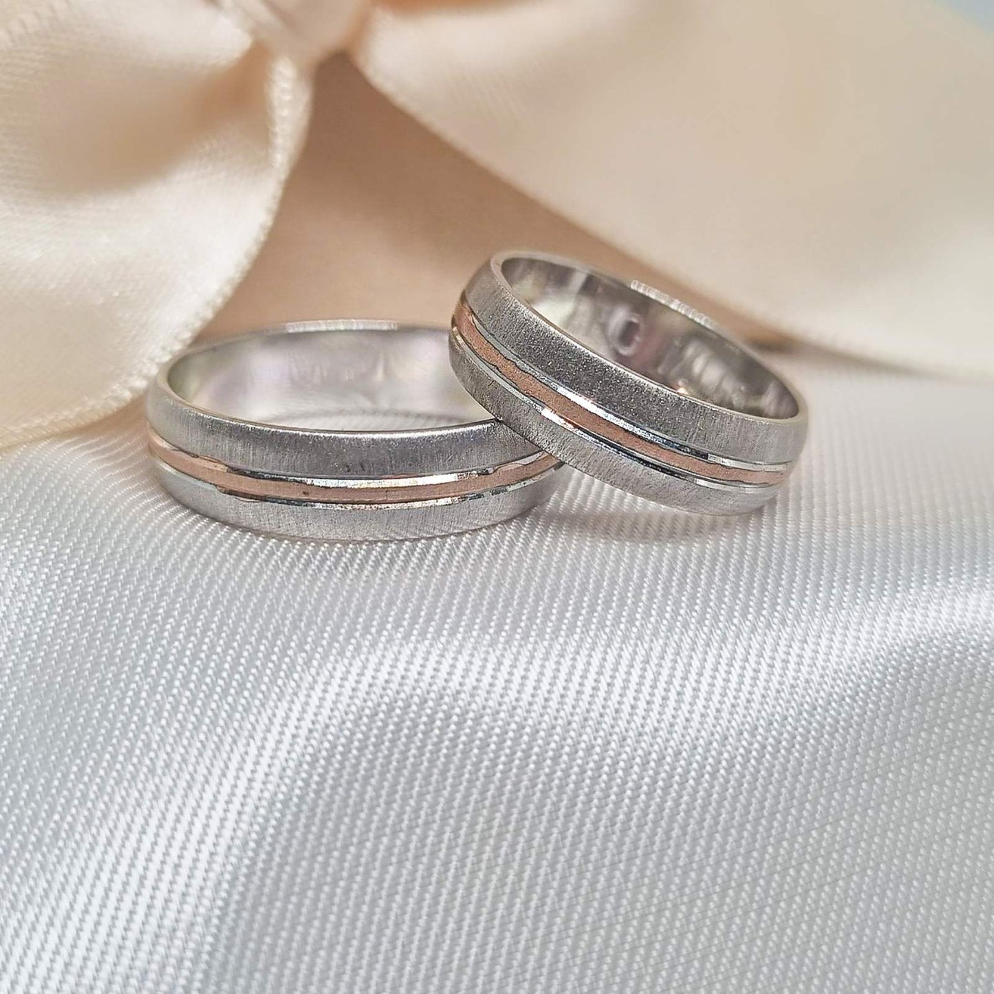 Zlatne burme sa matiranim i poliranim dizajnom, ukrašene tankim linijama u roze zlatu, postavljene na bež tkanini sa svetlom pozadinom.