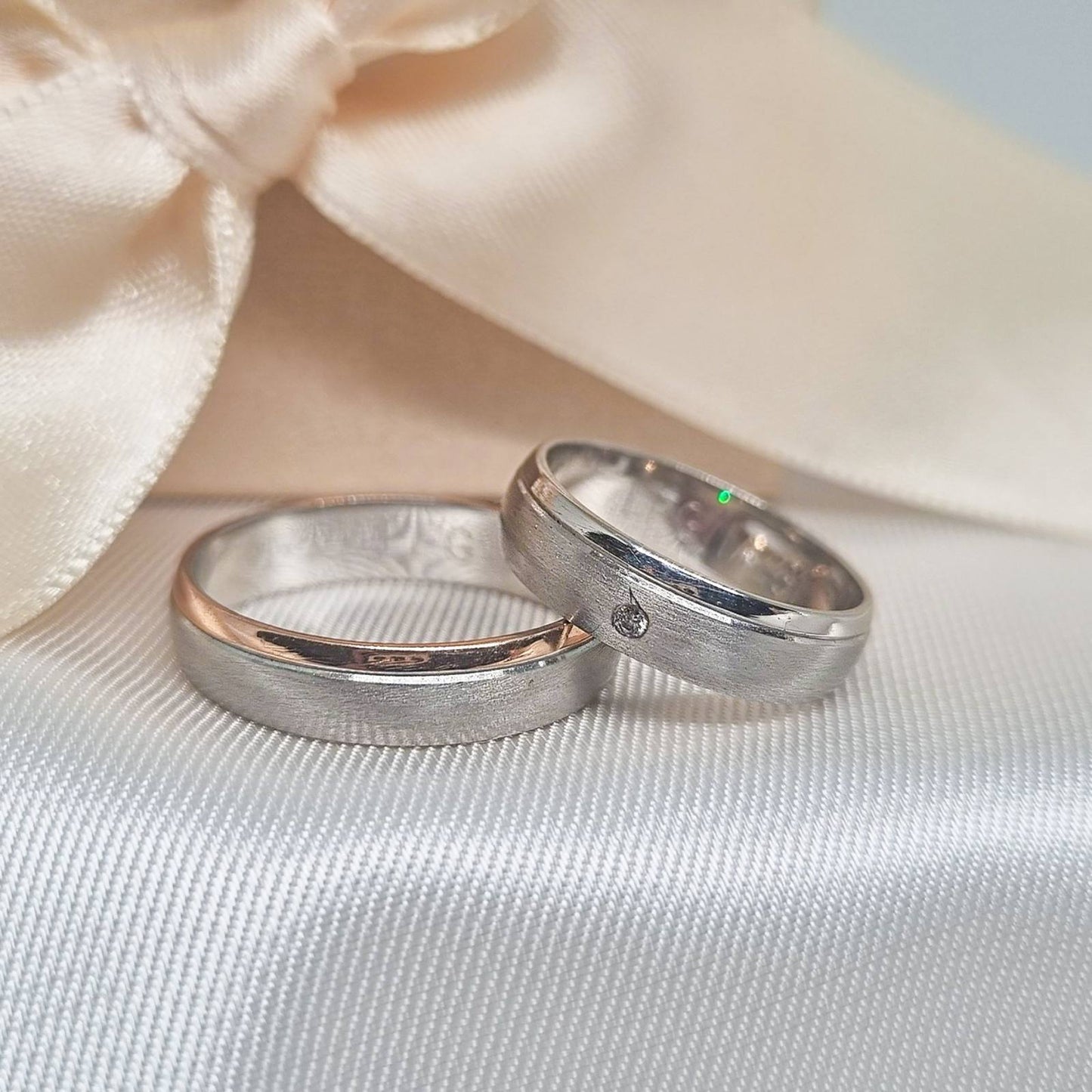 Zlatne burme od belog zlata sa matiranom površinom, jedna sa cirkonom, postavljene na svetloj tkanini sa bež pozadinom.