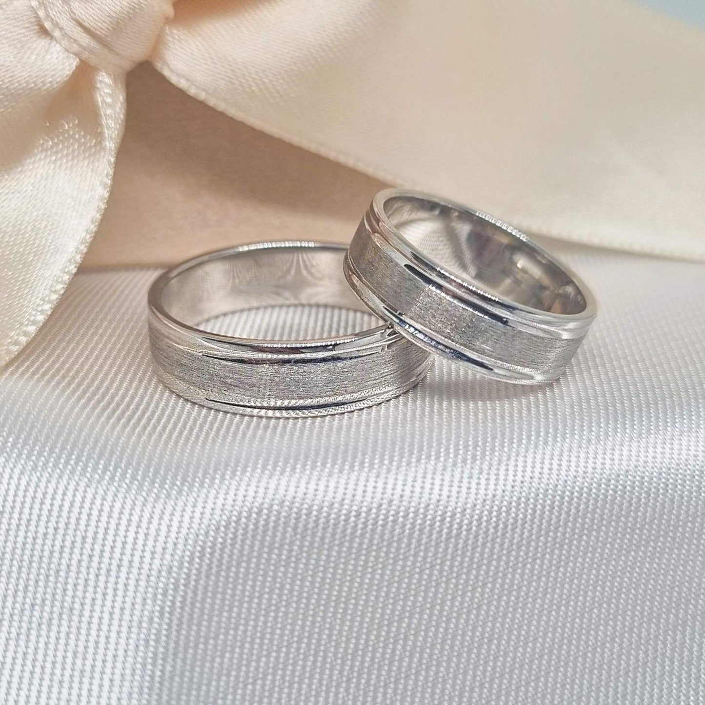 Zlatne burme sa matiranim i poliranim prugama, postavljene na bež tkanini sa svetlom pozadinom.