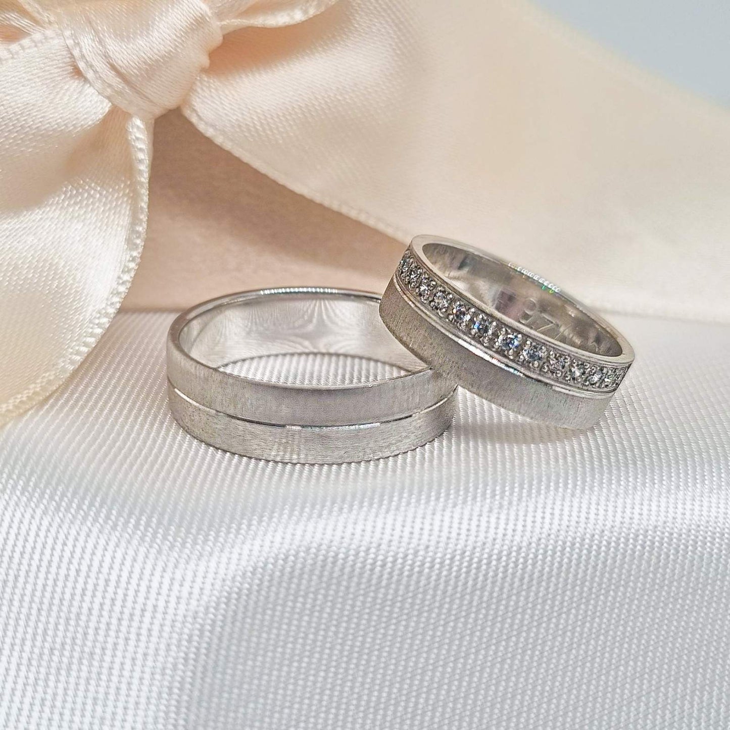 Zlatne burme sa matiranim i poliranim površinama, jedna ukrašena sa cirkonima, postavljene na bež tkanini sa svetlom pozadinom.